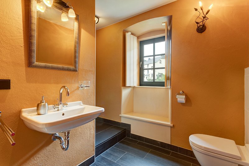 Ein geräumiges Badezimmer mit Spiegel, Waschbecken, WC und Armatur.