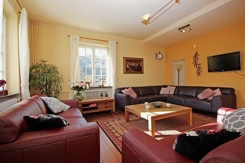 Gemütliches Wohnzimmer mit bequemer Couch, Tisch und Fenster mit Holzrahmen.