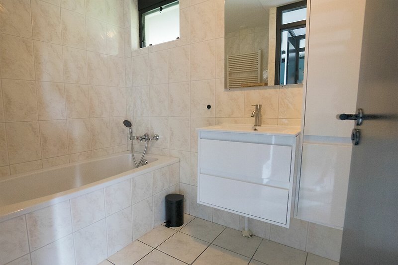 Modernes Badezimmer mit Spiegel, Fenster, Waschbecken und Armatur.