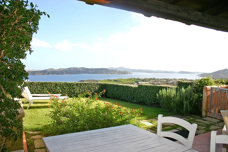 Sonnige Terrasse mit Meerblick, Outdoor-Möbeln und großem Esstisch.