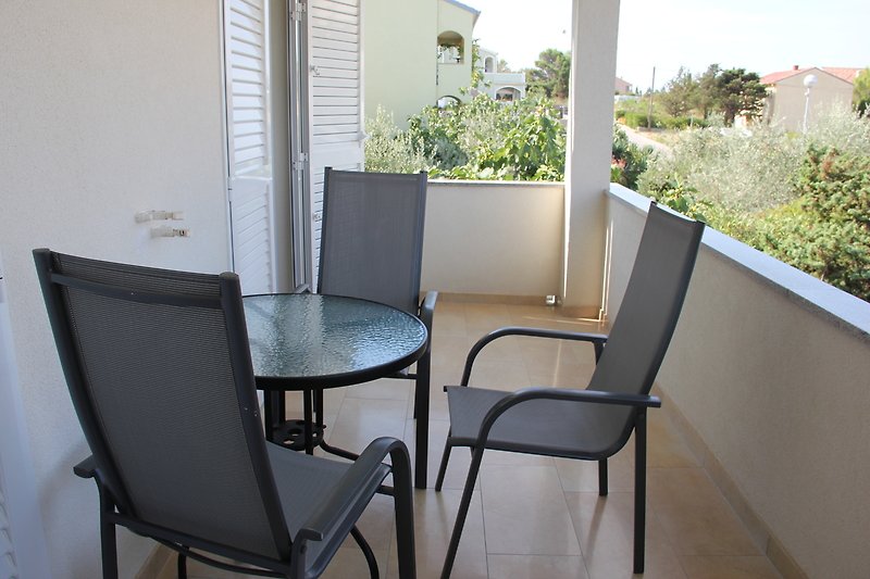 Balkon mit Stühlen, Tisch, Pflanzen und Blick auf Haus. Gemütliche Atmosphäre.