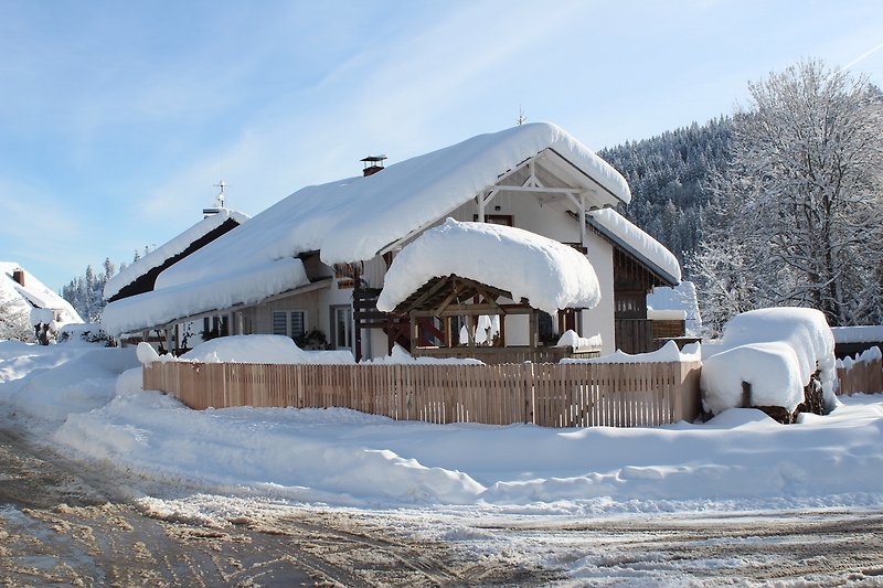 Luxuriöses Haus mit schneebedecktem Dach, umgeben von winterlicher Landschaft und majestätischen Bäumen.